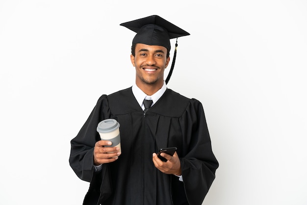 持ち帰り用のコーヒーと携帯電話を保持している孤立した白い背景の上のアフリカ系アメリカ人の大学卒業生の男