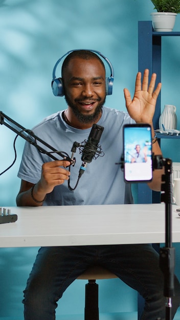 African american vlogger using smartphone to film podcast in studio. Black blogger with mobile phone, microphone and headphones filming video for social media broadcasting career.