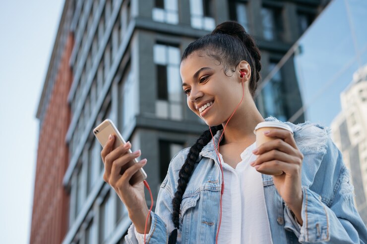 Foto african american vrouw met behulp van mobiele telefoon, kopje koffie houden, luisteren naar muziek