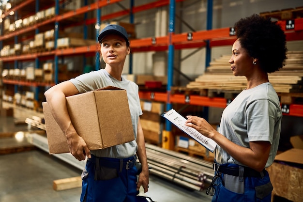african american warehouse worker and her colleague talking in storage compartment
