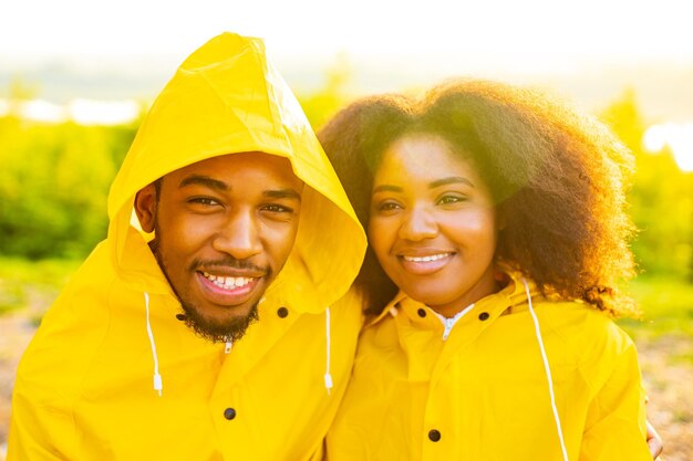 African american wife and husband in yellow raincoat with a hood feeling happy at sunset outdoors summer rain drop