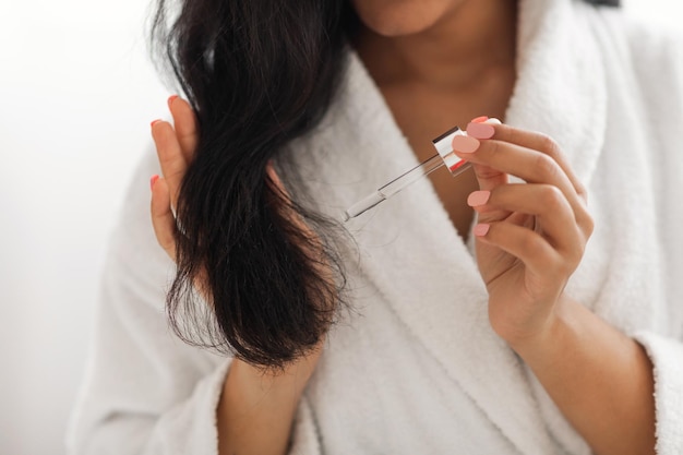 African American Woman Applying Serum On Hair Indoors Cropped