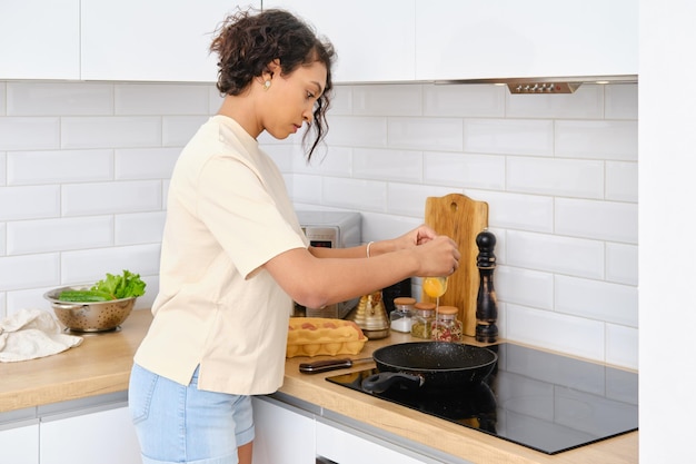 African american woman breaking egg in frying pan at home