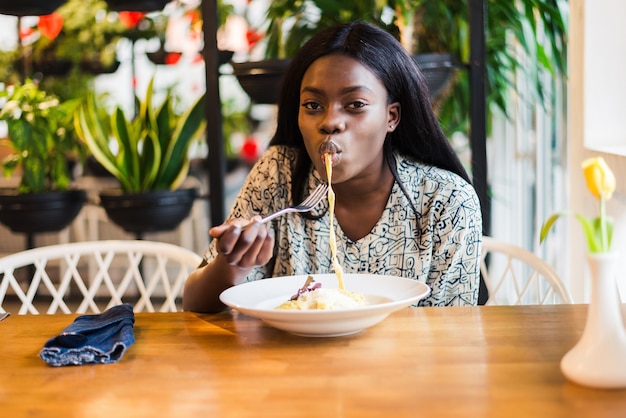 カフェでアフリカ系アメリカ人の女性がスパゲッティパスタを食べる