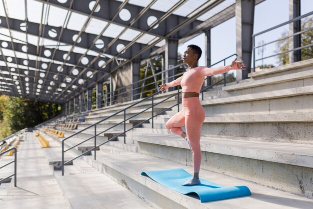 African American woman doing yoga near the stadium in the morning, active lifestyle performs fitness exercises