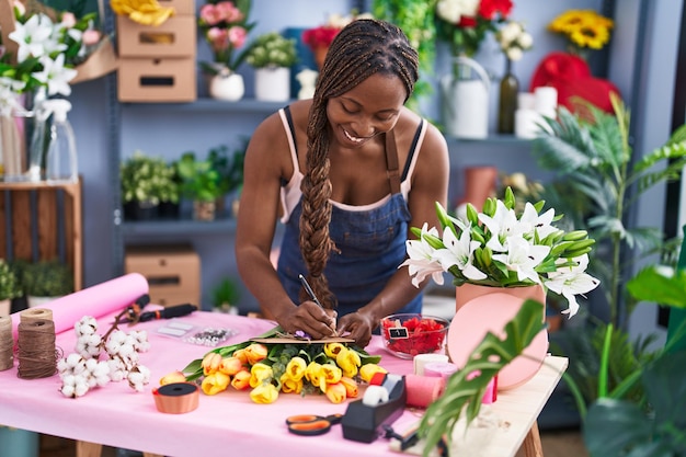 African american woman florist smiling confident writing on envelope letter at flower shop