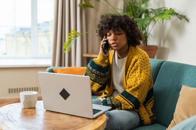 African american woman freelancer using laptop talking on phone at home office happy business girl