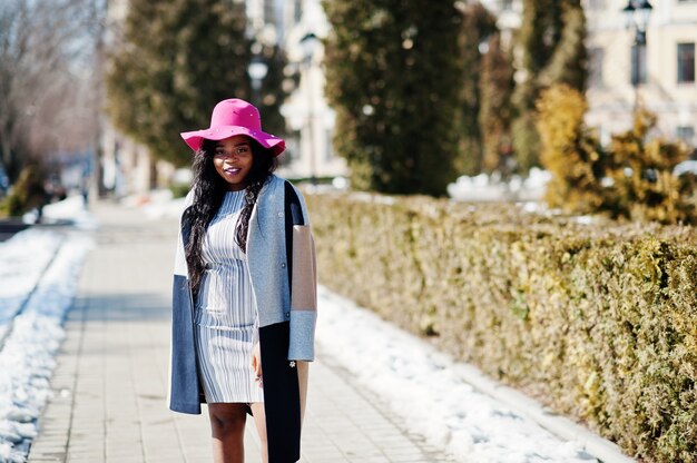 African american woman at hat and coat with phone walking at streets.