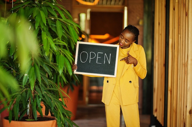 La donna afroamericana tiene aperta il cartello di benvenuto nella moderna caffetteria caffetteria pronta al servizio, ristorante, negozio al dettaglio, proprietario di una piccola impresa.