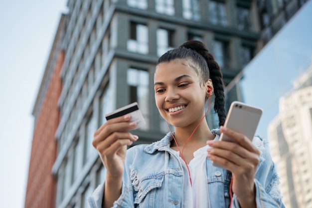 アフリカ系アメリカ人の女性がクレジットカードを保持している、スマートフォンを使用して、オンラインショッピング