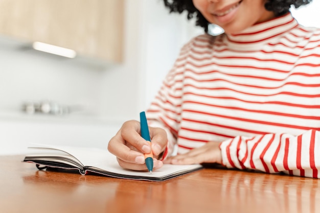 Photo african american woman holding pen taking notes in notebook sitting at desk