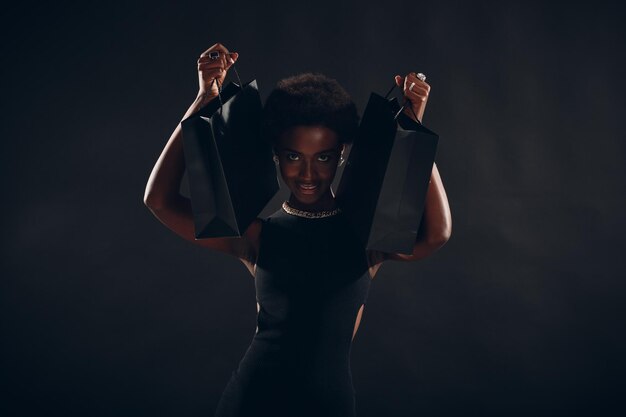 Photo african american woman holds black shopping bags sale and discounts on market and black friday concept