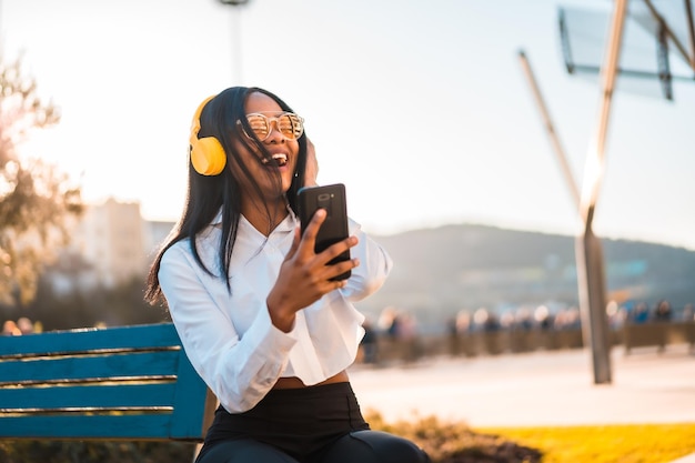 African american woman listening to music and smiling with headphones in the summer at sunset in the city