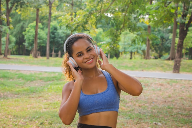 Photo african american  woman listening to music with headphones and smiling in park.