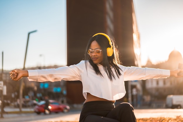 온라인 도시 음악에서 일몰에 헤드폰으로 음악을 듣고 춤을 추는 아프리카계 미국인 여성
