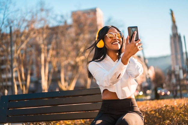 African american woman listening to music with headphones at sunset in the city