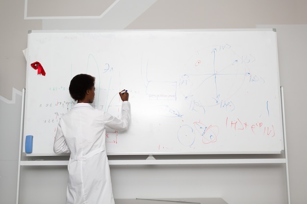 African American woman math teacher stands at blackboard with marker