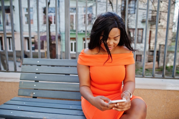 휴대 전화를 보고 오렌지 드레스에 아프리카계 미국인 여자 모델 Xxl
