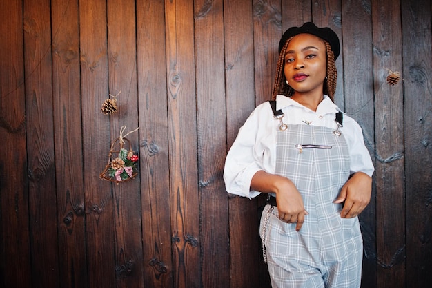 African american woman in overalls and beret against wooden wall