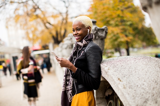 Donna afroamericana che posa fuori con il telefono cellulare e una tazza di caffè per andare in autunno