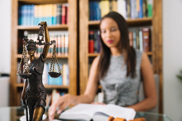 African American woman reading book at table with statue in office