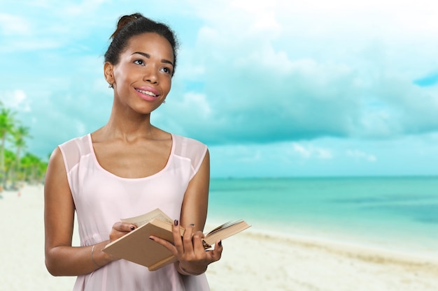 African american woman reading a novel book on the beach, summer holidays