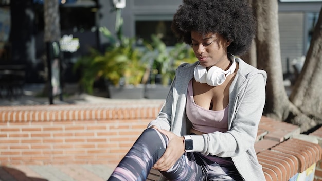 African american woman sitting on bench for injury knee at park