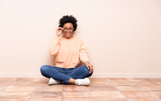 African american woman sitting on the floor with glasses and surprised