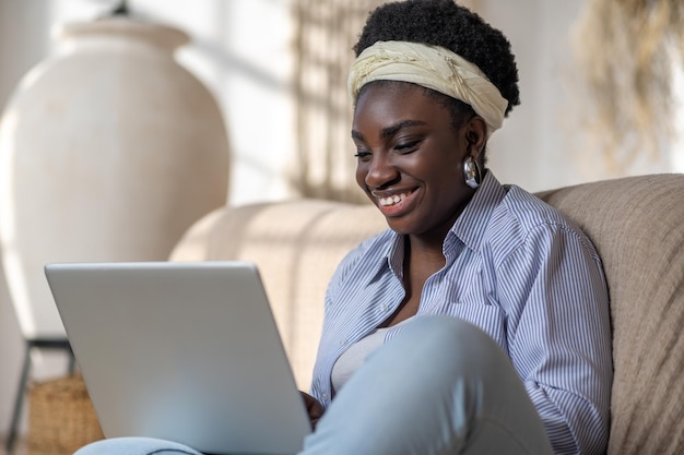 소파에 앉아 온라인 채팅을 하며 시간을 보내는 아프리카계 미국인 여성