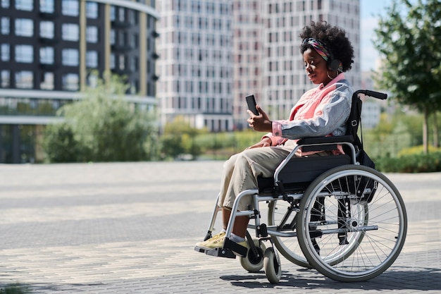 African American woman sitting in wheelchair and using smartphone during her walk in the city