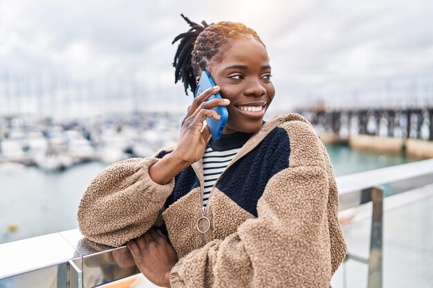 海辺でスマートフォンで話す自信に満ちた笑顔のアフリカ系アメリカ人女性