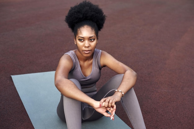 Афроамериканка в спортивной одежде отдыхает на стадионе после бега или тренировки
