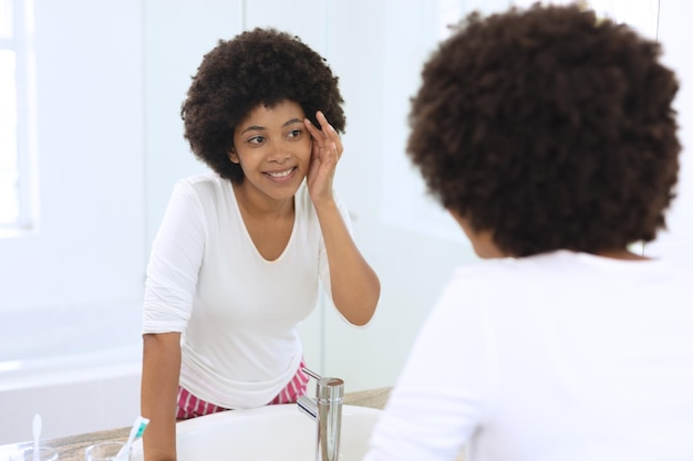 African american woman standing in bathroom applying face cream