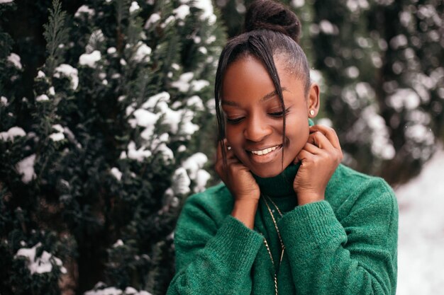 Donna afroamericana in piedi fuori strada vicino all'albero di natale, vestito caldo maglione verde