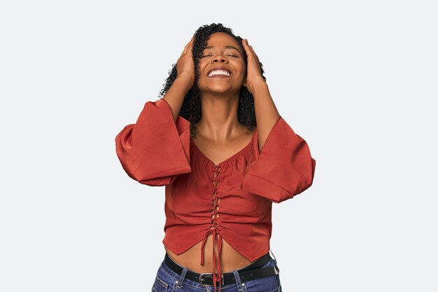 African American woman in studio setting laughs joyfully keeping hands on head Happiness concept