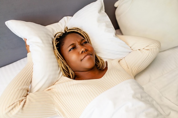 Donna afroamericana che cerca di dormire ma il rumore la infastidisce, sta coprendo le orecchie con un cuscino