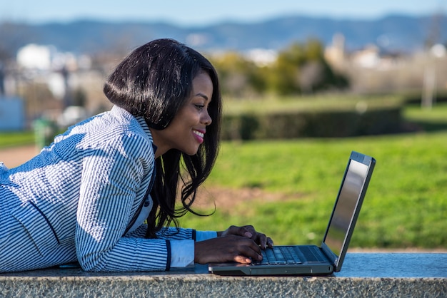 Donna afroamericana che utilizza un computer portatile in un parco all'aperto