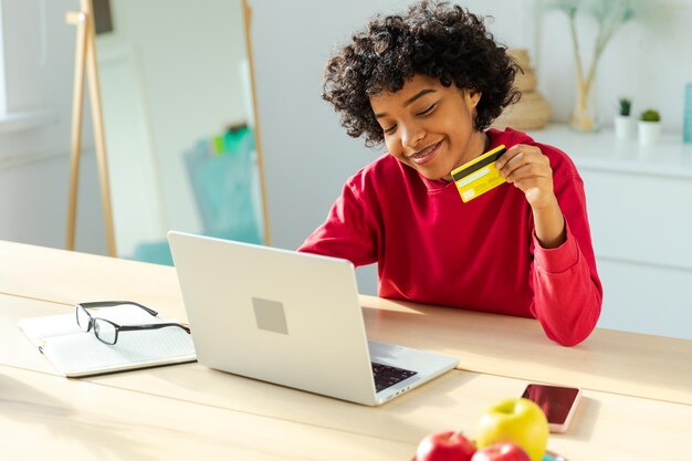 African american woman using laptop shopping online paying with gold credit card girl sitting at