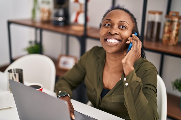 African american woman using laptop talking on the smartphone at home