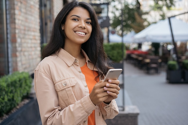 African american woman using mobile phone, standing on the street, waiting for taxi