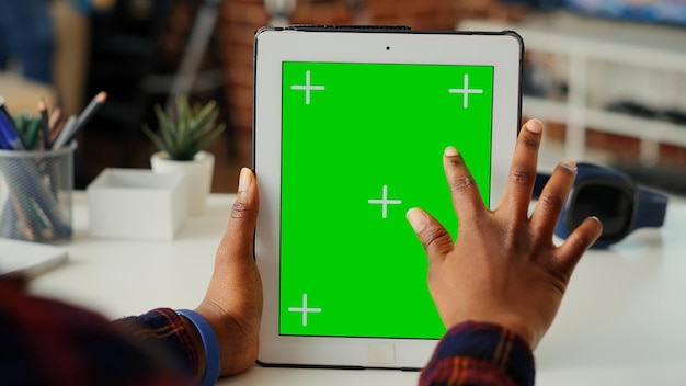African american woman vertically holding isolated greenscreen\
on digital tablet, looking at blank chroma key display with mockup\
background. using copy space on portable device. close up.