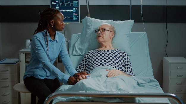 african american woman visits sick patient in hospital ward bed at medical facility old man with oxi...
