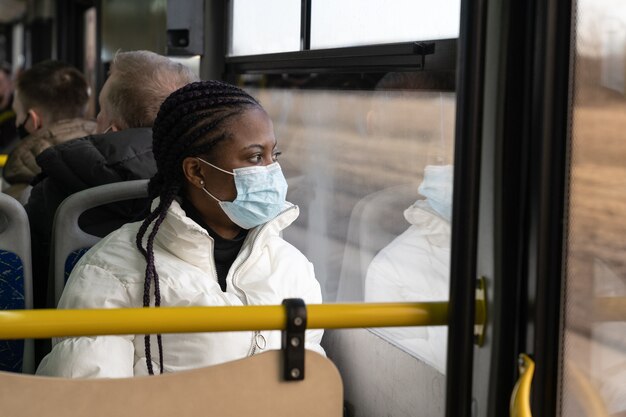 La donna afroamericana indossa una maschera medica viaggia in autobus di trasporto pubblico nella nuova normalità di covid