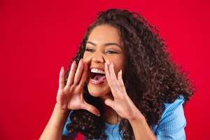 African american woman wearing a blue t-shirt over isolated red background shouting and screaming loud to side with hand on mouth. communication concept.