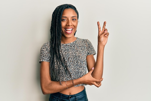 African american woman wearing casual clothes smiling with happy face winking at the camera doing victory sign. number two.