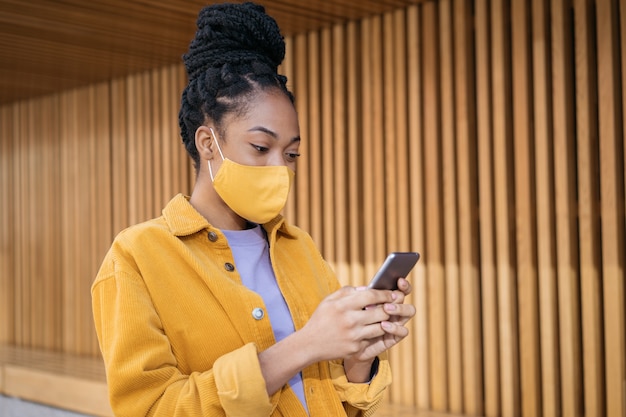 Photo african american woman wearing protection face mask using mobile phone communication online