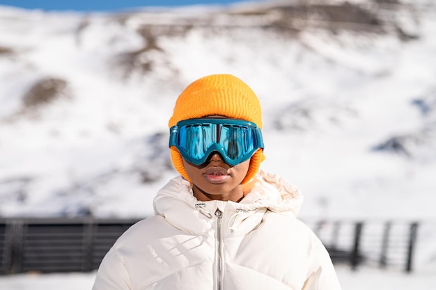 Афроамериканка в снежных очках на заснеженной горе зимой.