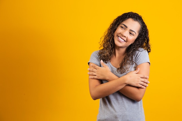 African American woman with afro hair, wearing a casual t-shirt, hugging herself happy and positive, smiling confidently. self love and self care