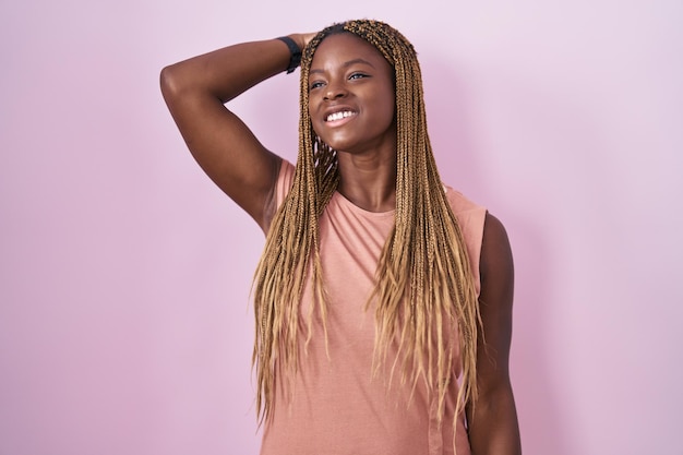 African american woman with braided hair standing over pink background smiling confident touching hair with hand up gesture posing attractive and fashionable