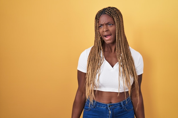 Photo african american woman with braided hair standing over yellow background angry and mad screaming frustrated and furious shouting with anger rage and aggressive concept